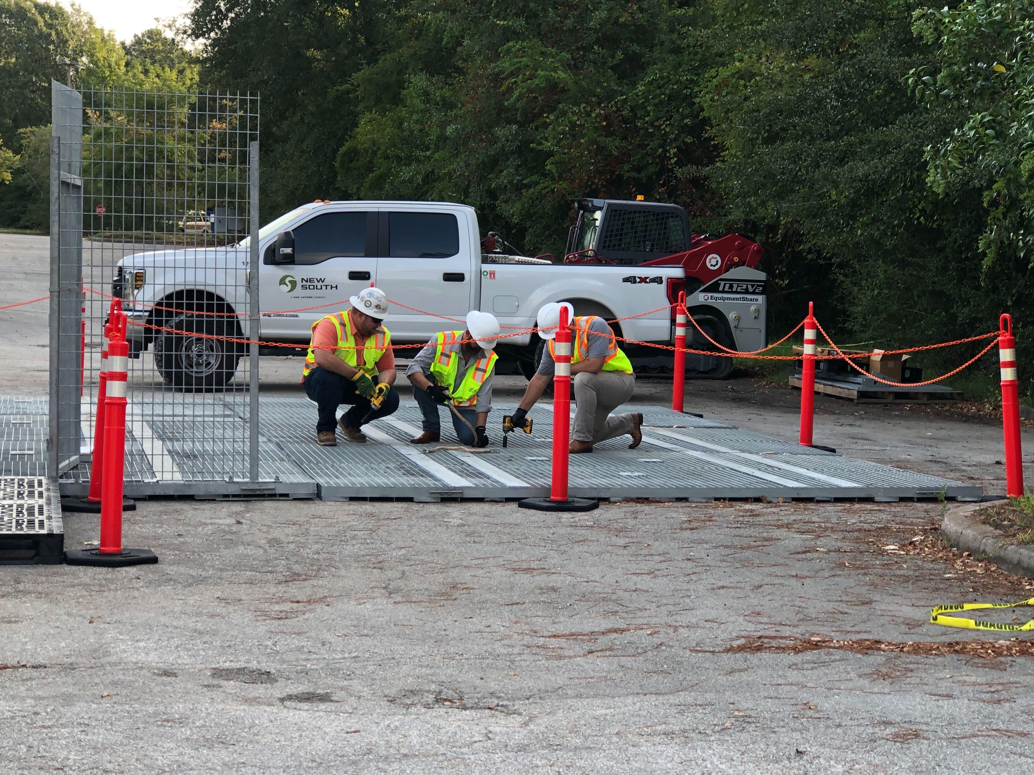 Construction crew sets up temporary matting and barriers around powerline work area.