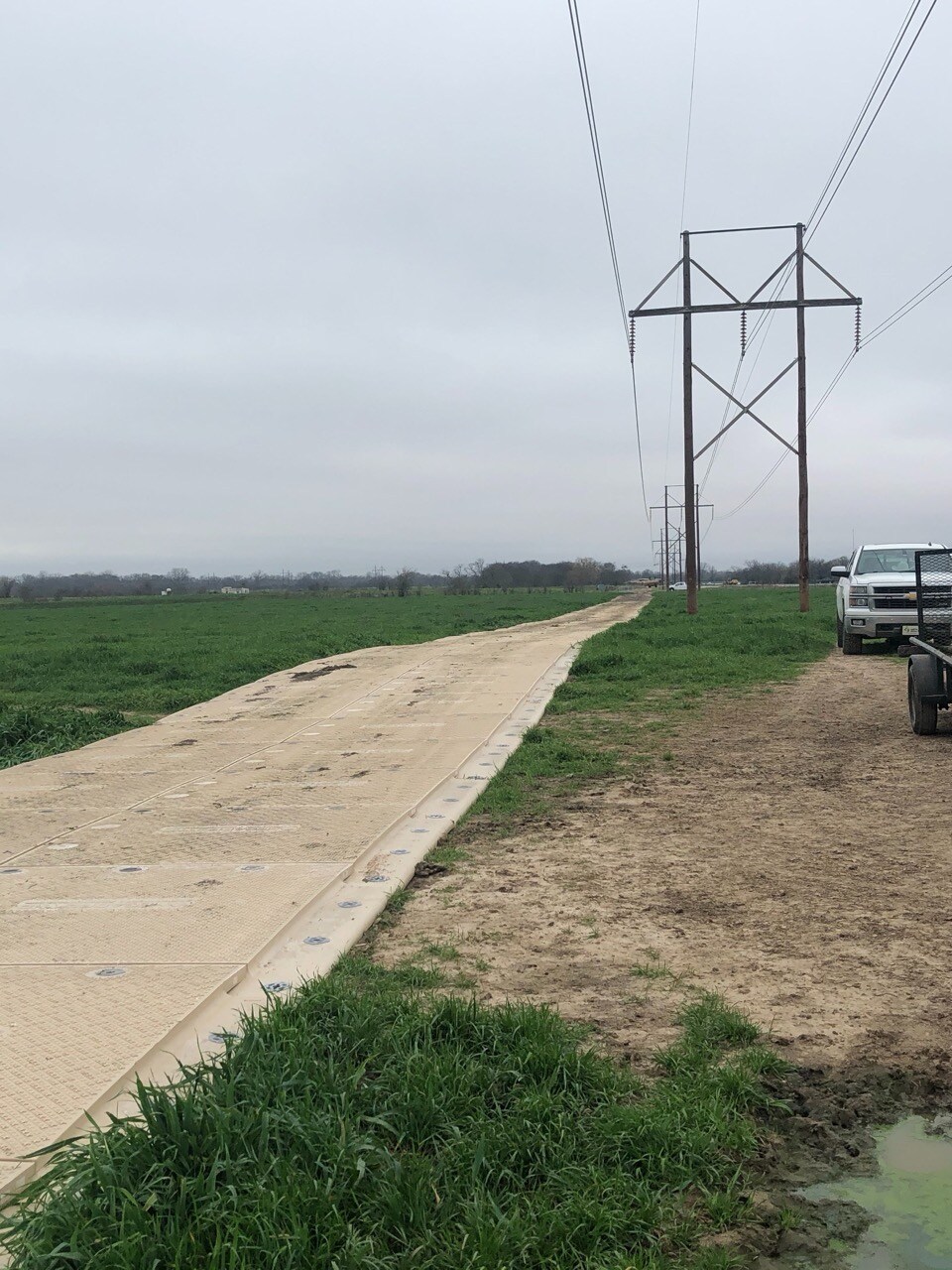 Dirt path with a row of interlocked composite mats leading towards a utility pole in a grassy field.